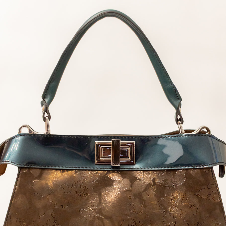 Close-up image of Charlotte handbag in Bronzo Fiore featuring teal accent trim and matching structured top handle