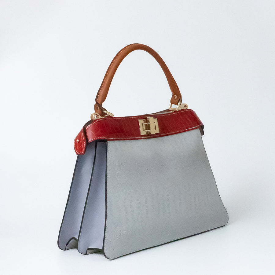 Angled image of Charlotte handbag in Neve Rossa featuring structured accordion side panels with white Italian leather and structured top handle
