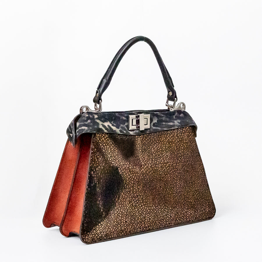 Angled image of Charlotte handbag in Tuscan Bronze featuring structured accordion side panels with red textured Italian leather