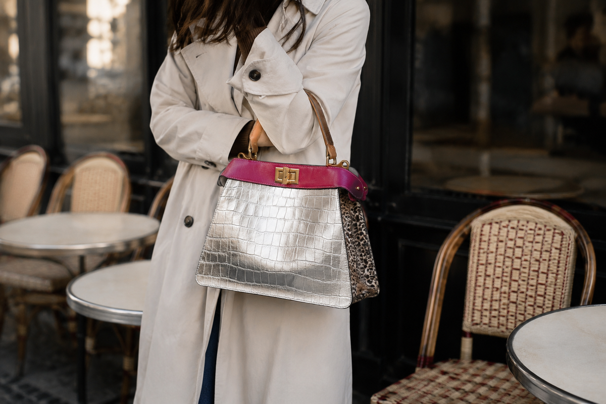 Person in trenchcoat holding Charlotte handbag in Villa Rosa in an outdoor cafe setting