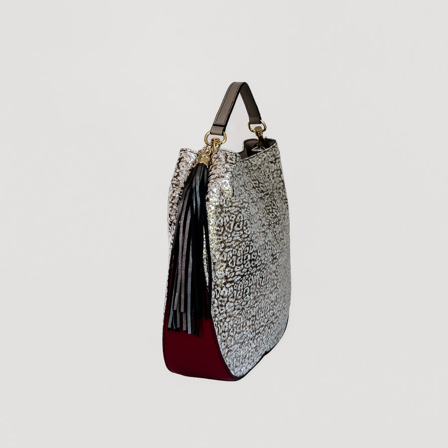 Side view of Lily handbag in Lunaria featuring black tassel and handle and maroon leather bottom
