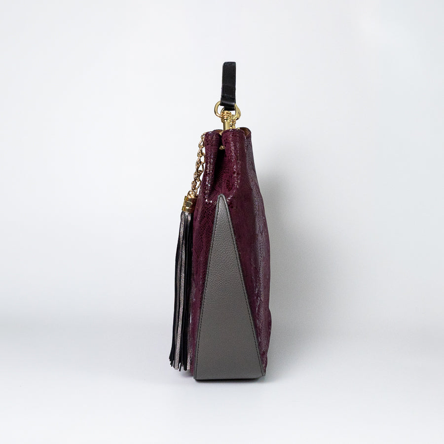 Side view of the Lily handbag in Midnight Fig featuring grey leather bottom and black leather tassel and strap